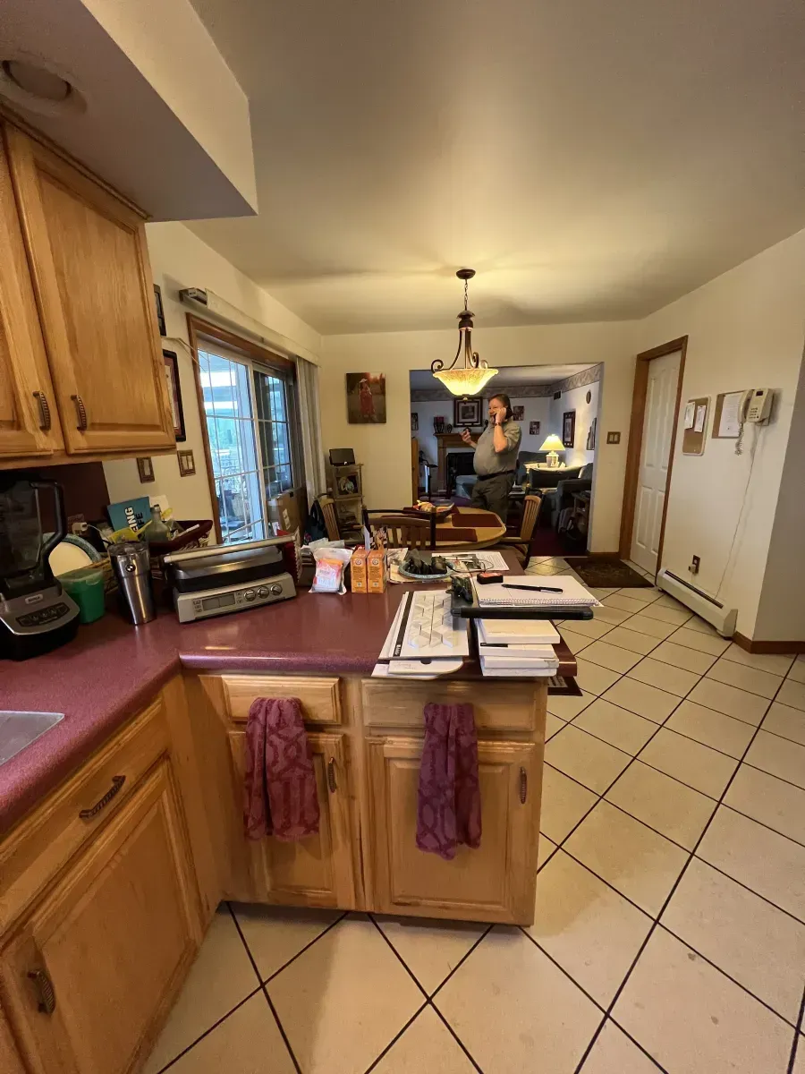 Kitchen with wooden cabinets, tiled floor, island, and pendant lights; a person stands near the back counter.