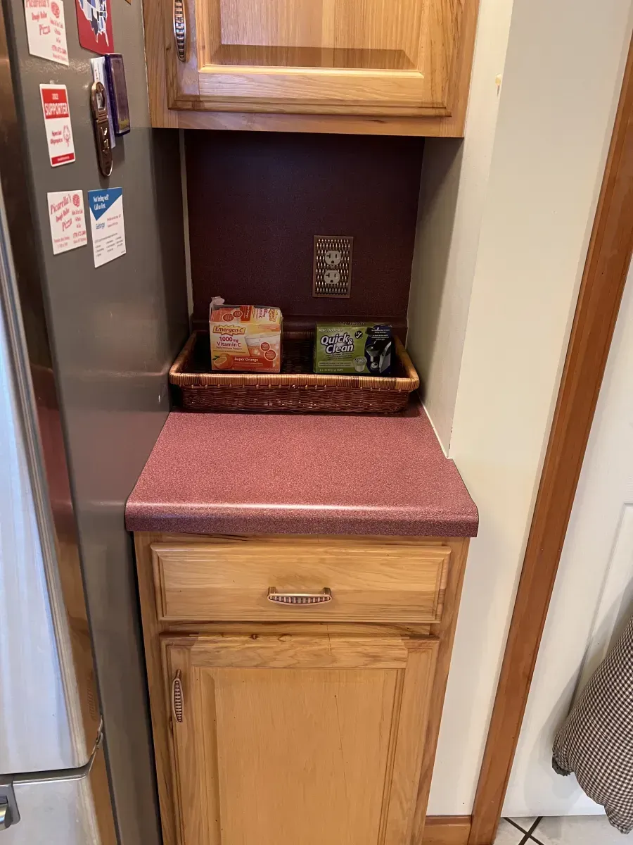 Kitchen pantry nook with red countertop, wood cabinets, and snacks on a shelf.