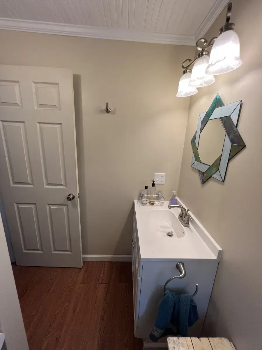 Small bathroom with white vanity, wall mirror, and closed door on wood floor
