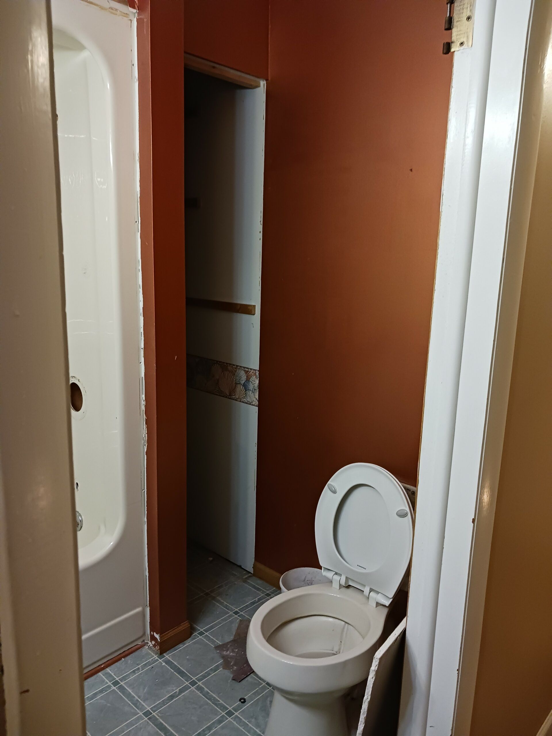Small bathroom with an open toilet, beige walls, and a doorway to another room.