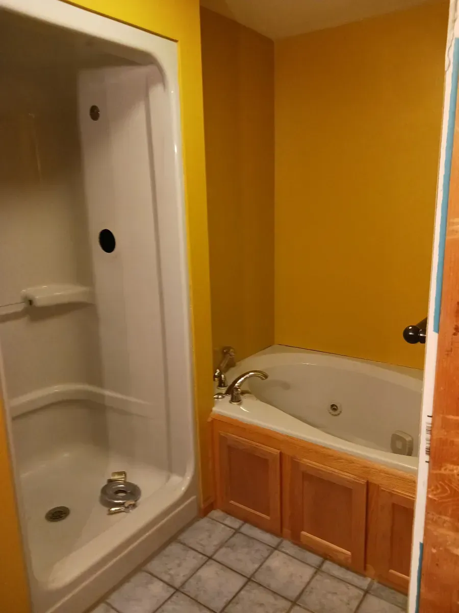 Small bathroom with yellow walls, a shower stall, and a built-in bathtub with wood cabinets.