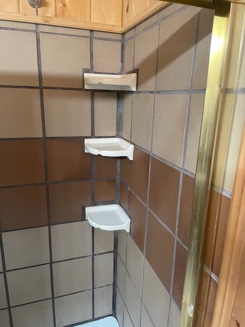 Corner shower shelf with three white corner shelves against tan and gray tiled walls.