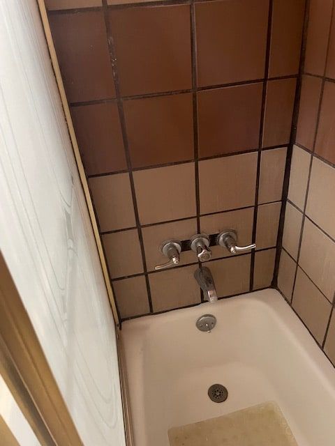 Compact bathtub with brown tiled wall and chrome faucet in a narrow bathroom.
