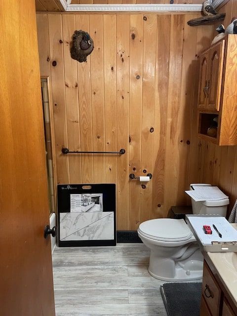 Small rustic bathroom with wood-paneled walls, toilet, sink, and framed prints on the floor.
