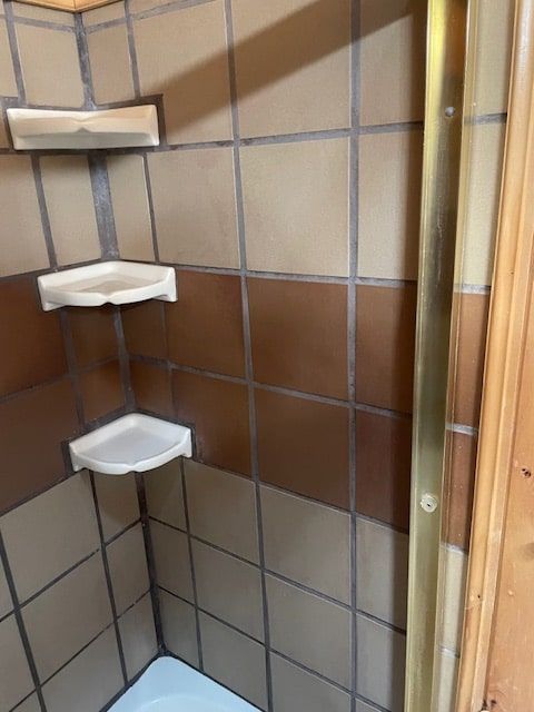 Corner shower with beige and brown tile and a white corner shelf unit