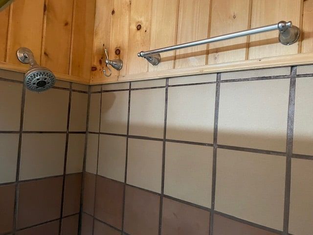 Tiled shower corner with wood-paneled wall, metal showerhead, and towel bar above the tiles