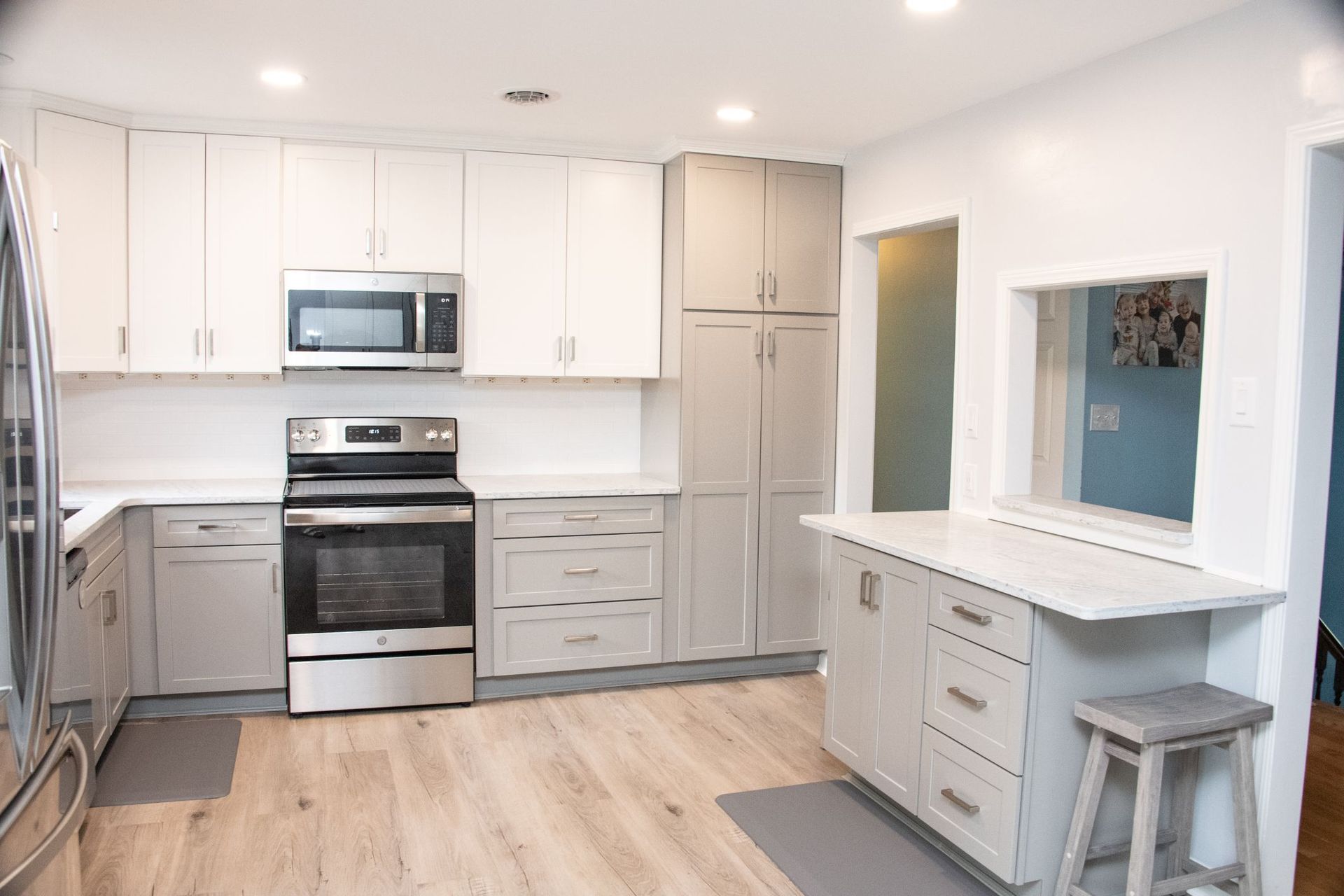 Bright white kitchen with stainless steel appliances, island, and light wood floor