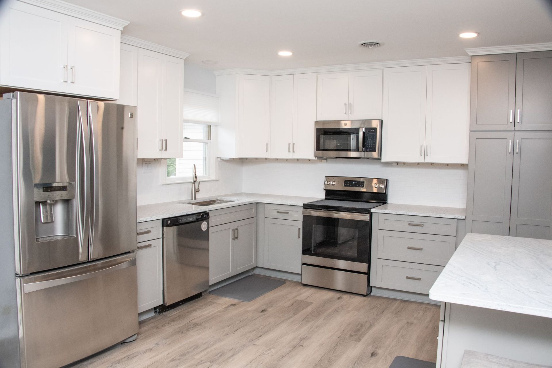 Bright white kitchen with stainless steel appliances, light wood floors, and a large island countertop