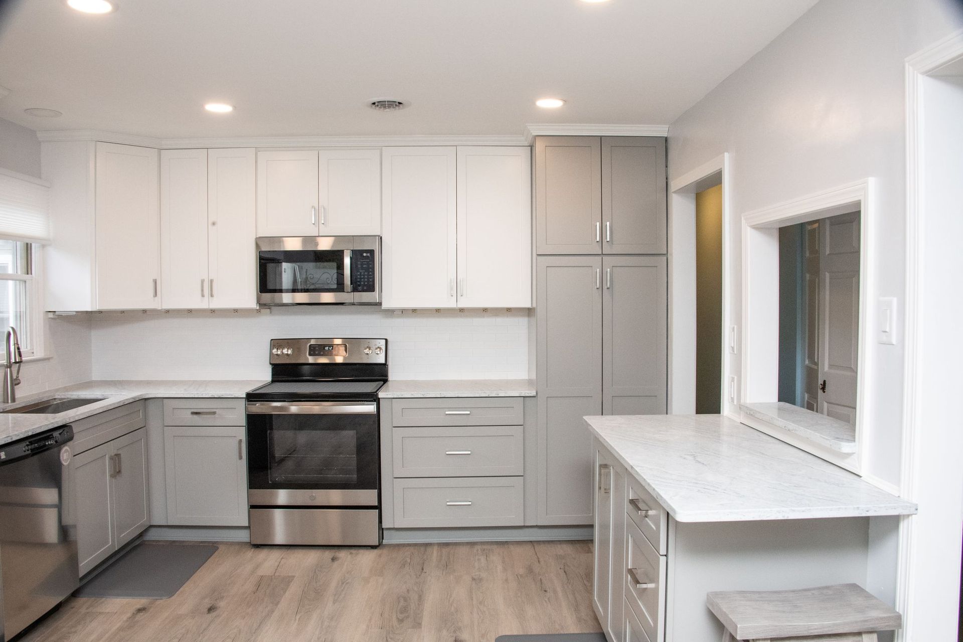 Modern white kitchen with stainless steel appliances, gray cabinets, and a small breakfast table by the window