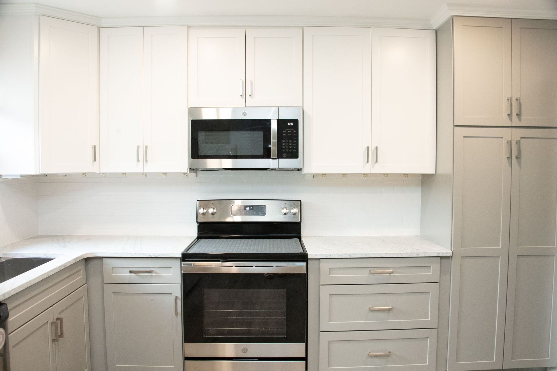 Modern white kitchen with stainless steel stove, microwave, and refrigerator along the back wall