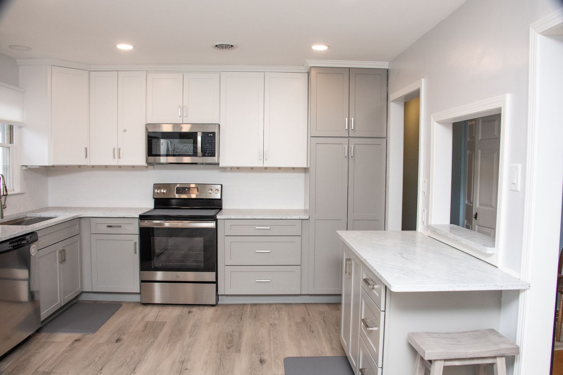 Bright white kitchen with stainless steel appliances, gray cabinets, wood floor, and a small breakfast counter.