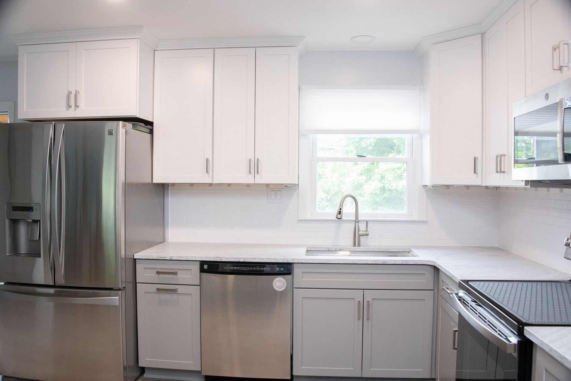 Bright modern kitchen with white cabinets, stainless steel appliances, and a window over the sink