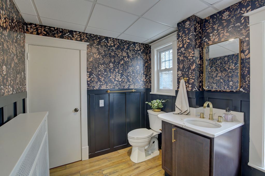 Modern bathroom with floral wallpaper, dark wainscoting, white vanity, toilet, and window light