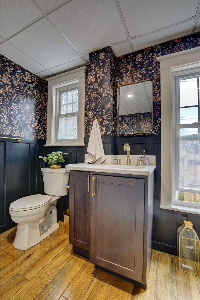 Small bathroom with dark wallpaper, white toilet, wood vanity, and tall windows on a hardwood floor