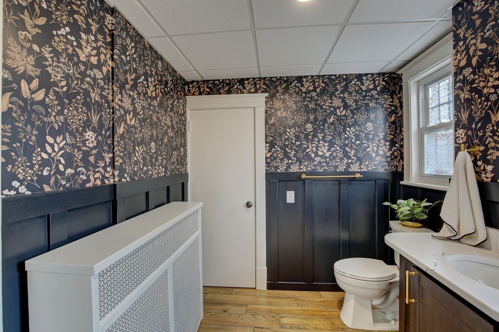 Bathroom with floral wallpaper, white toilet, dark vanity, and a window above the sink