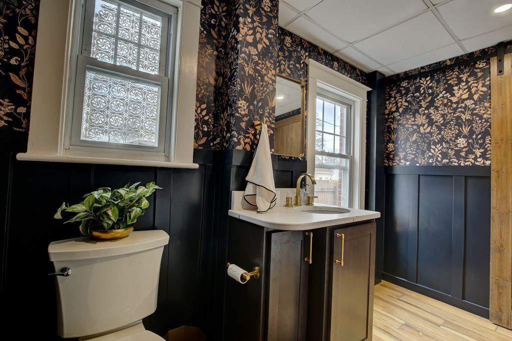 Small bathroom with black walls, floral wallpaper, pedestal sink, and a window.