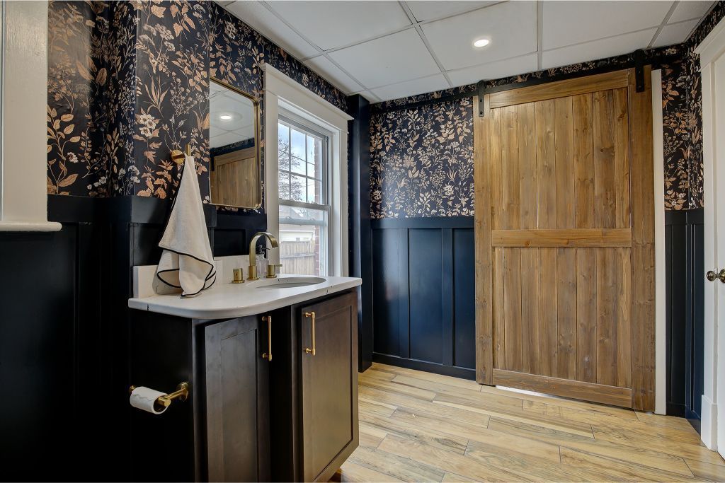 Small bathroom with dark walls, floral wallpaper, window, vanity sink, and wooden sliding door