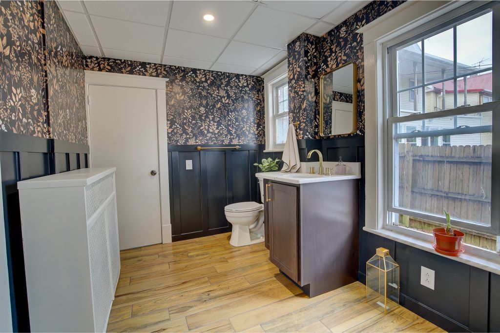 Bathroom interior with patterned wallpaper, white toilet, dark vanity, and window with blinds