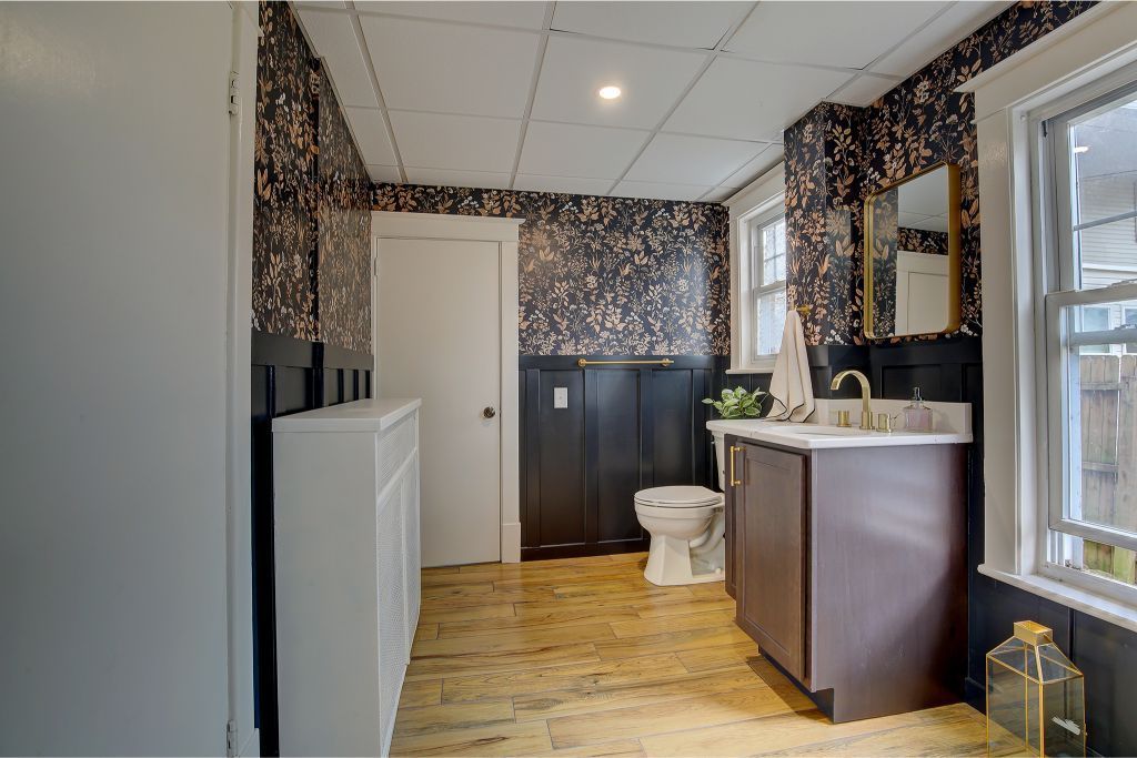 Small bathroom with dark wallpaper, white door, vanity, toilet, and window.