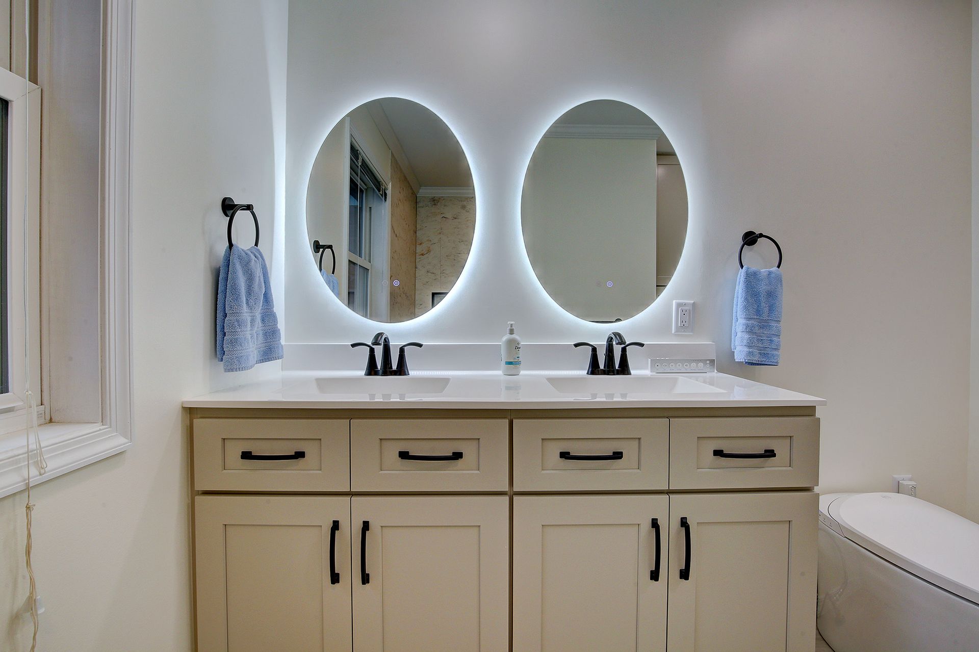 Modern bathroom vanity with double oval mirrors, cream cabinets, and soft backlighting