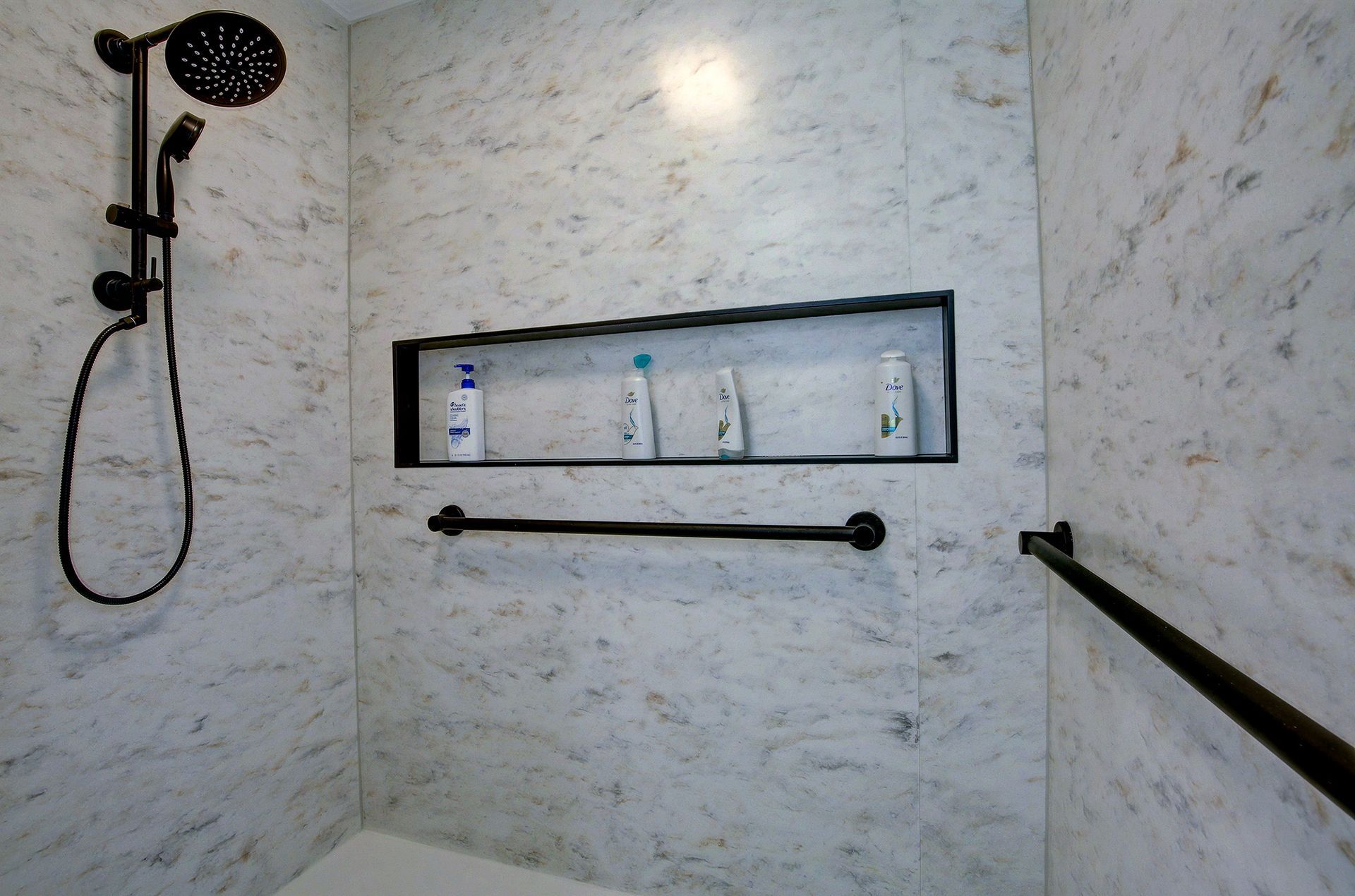 Modern tiled shower with black showerhead, recessed shelf, and safety grab bars