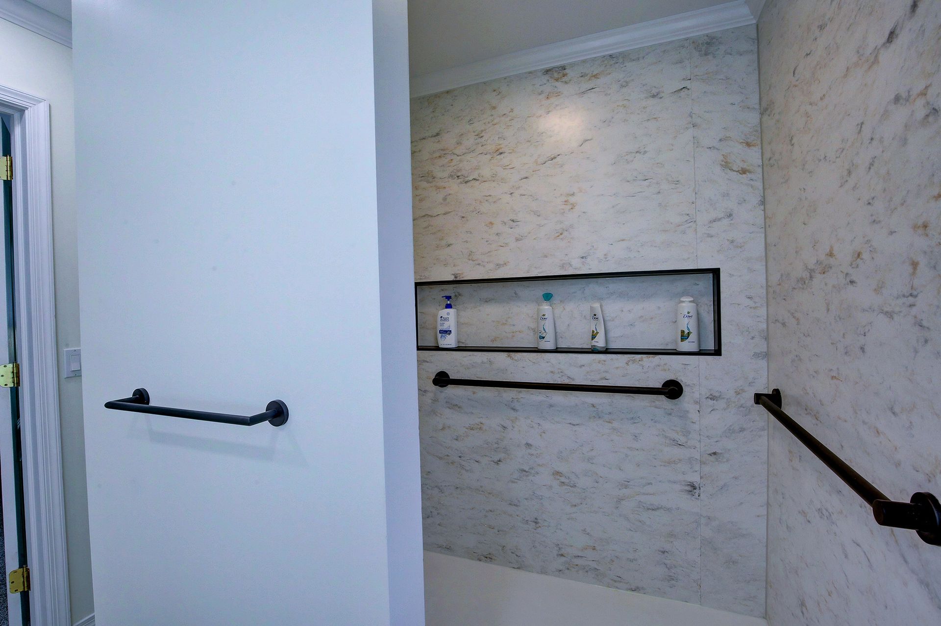 Accessible restroom stall with black grab bars and a built-in shelf on beige textured walls