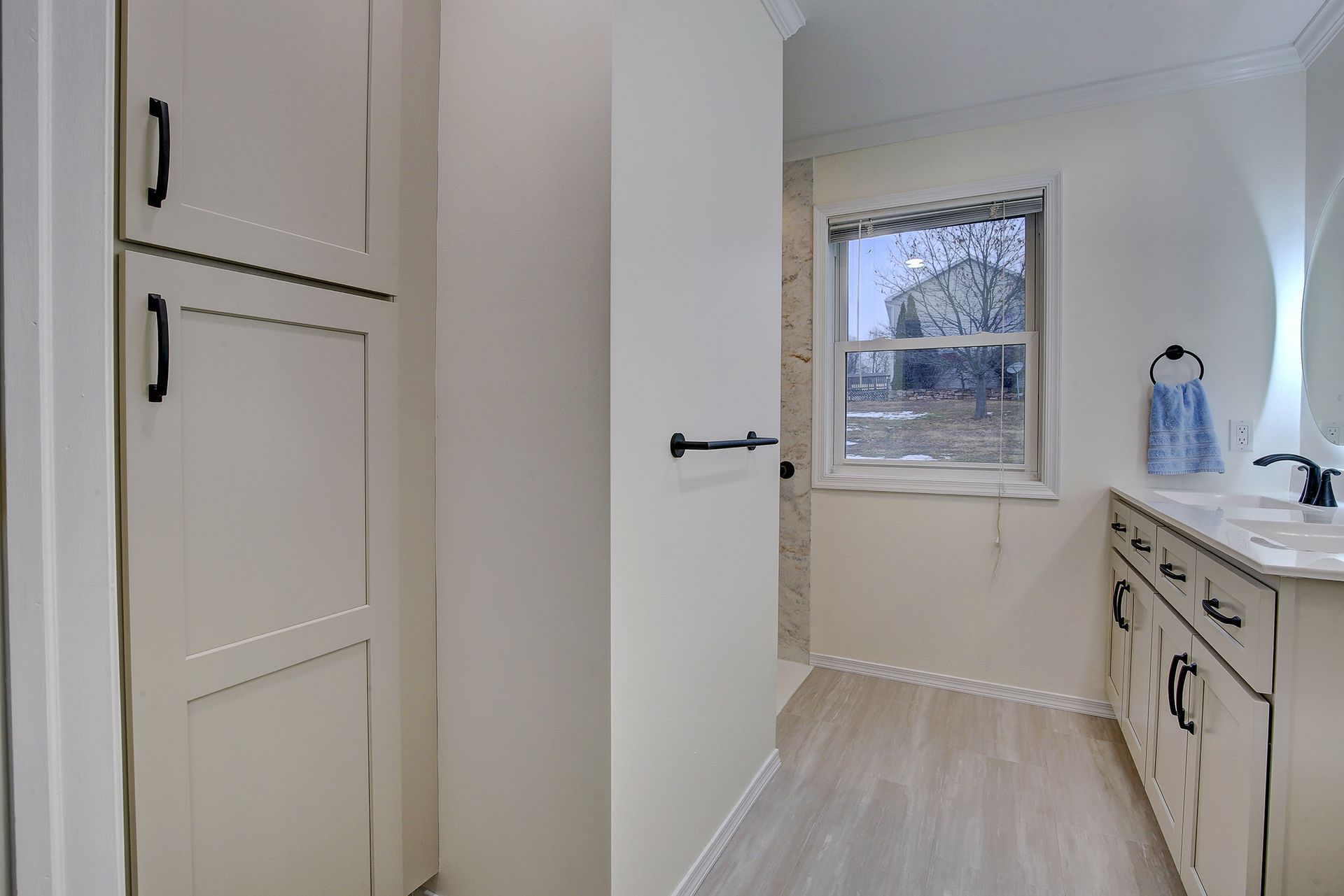 Bright white laundry room with cabinets, countertop, and a window overlooking snowy trees.
