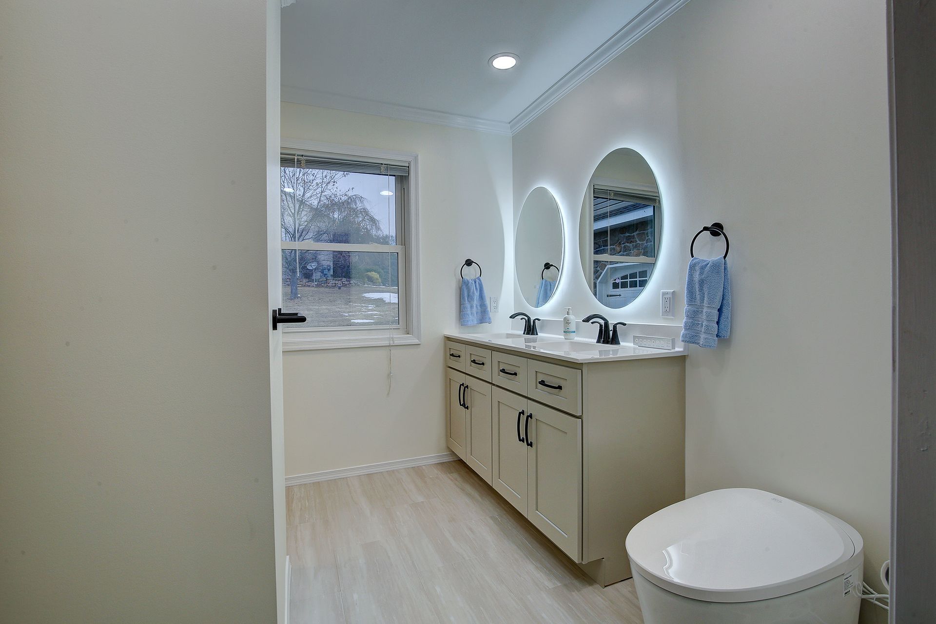 Bright bathroom with vanity, round mirror, window, and white toilet in a minimalist interior