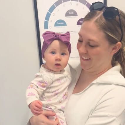 Woman holding a baby with a purple bow in a clinical office setting