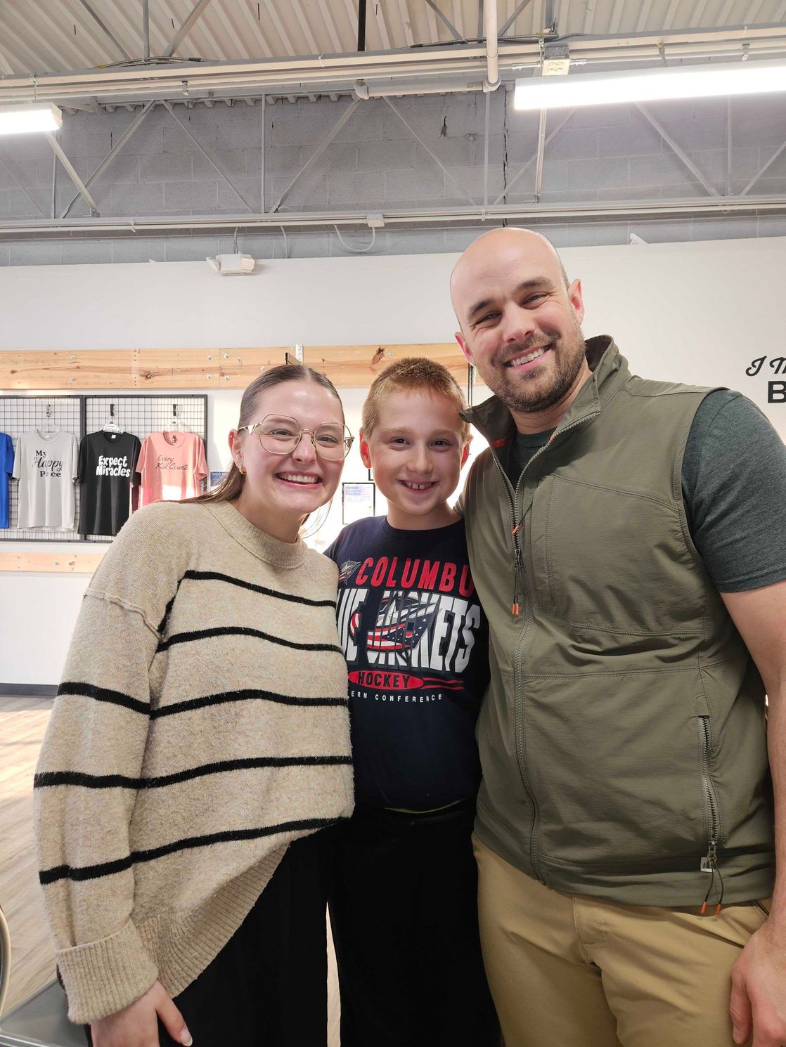 Three people smiling indoors, standing together in a store-like setting.