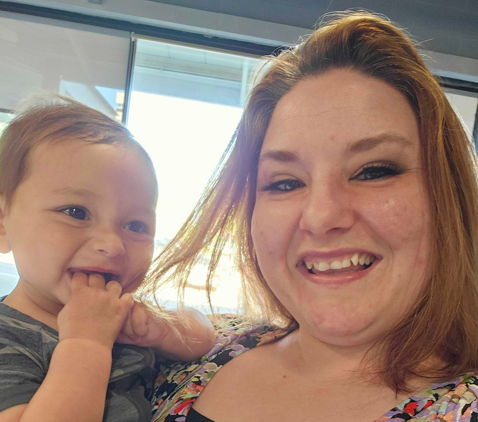Smiling adult and toddler posing indoors by a bright window
