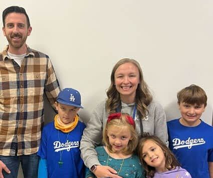 Family of six smiling in Dodgers shirts, standing against a plain wall.