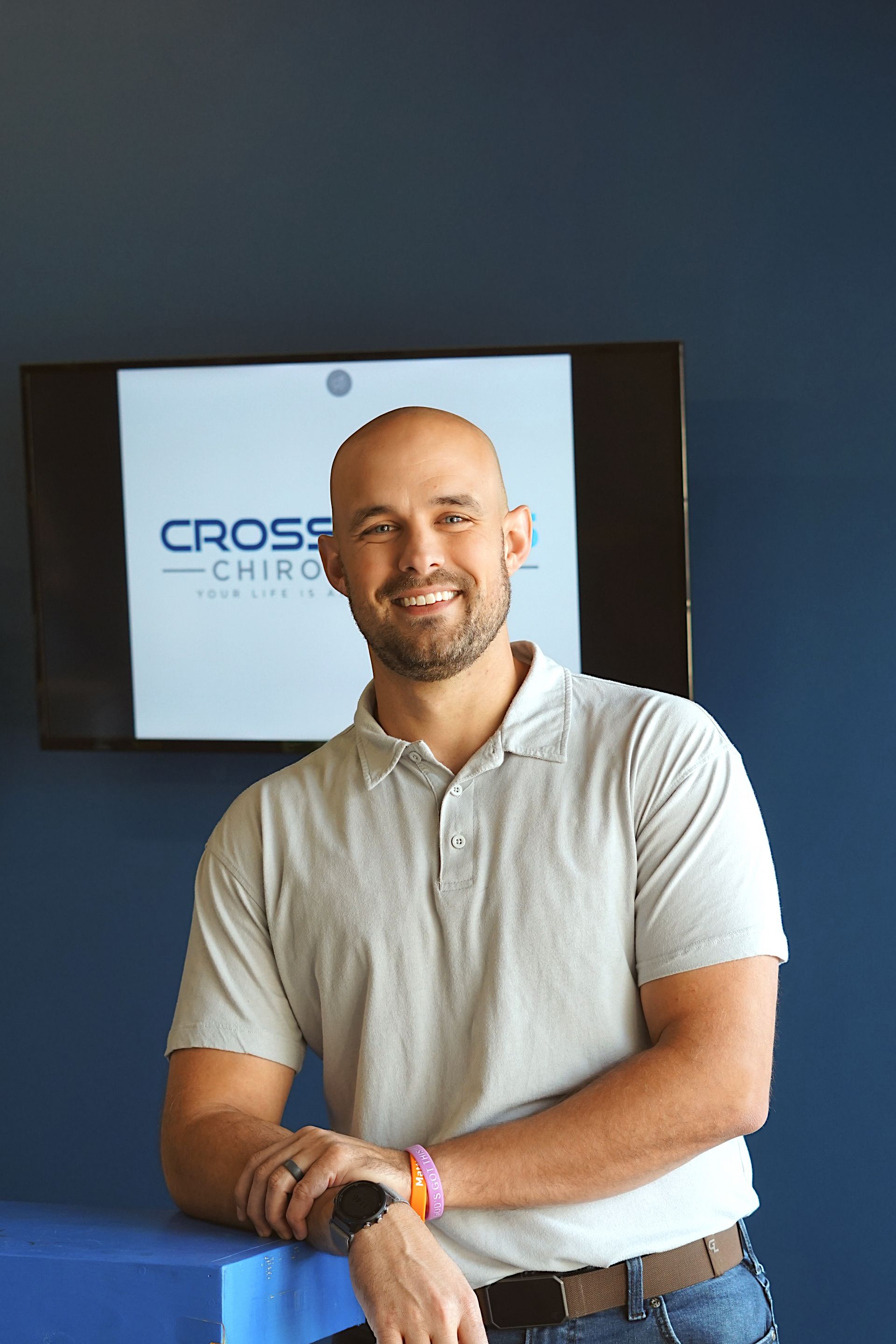 Smiling bald man in teal polo shirt standing before a stone wall