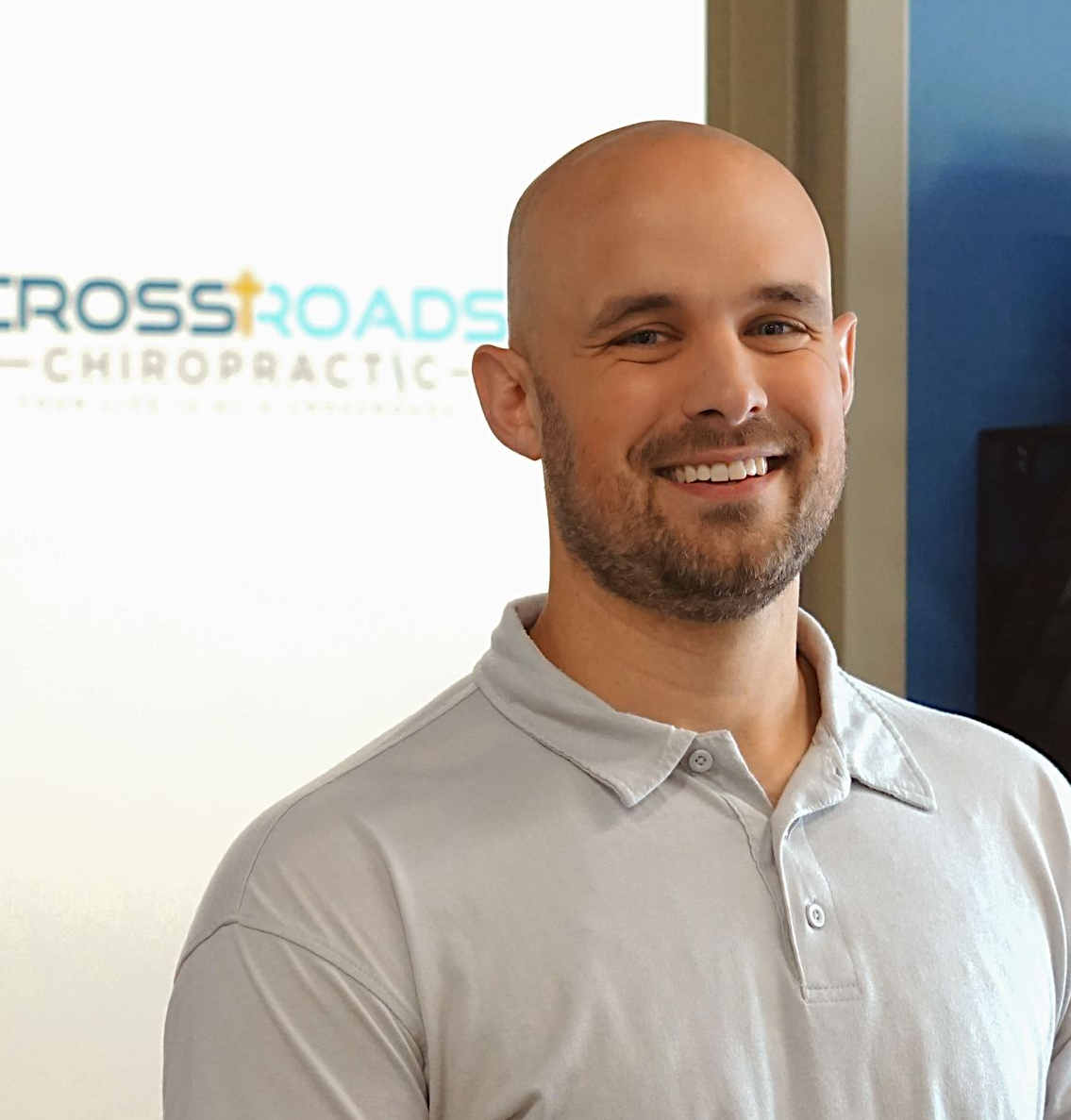Smiling bald man in a teal polo shirt standing before a stone wall.