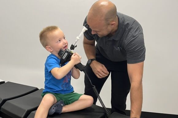Man helping a smiling child hold a cable in a clinic setting