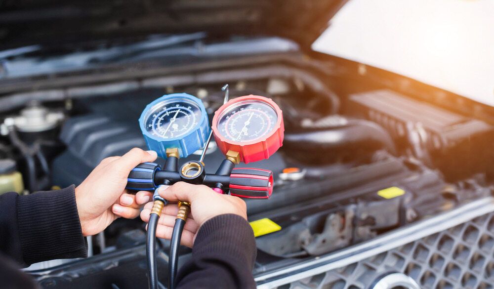 A Person is Holding Two Gauges in Front of a Car Engine — JJE Automotive In Yarrawonga, NT