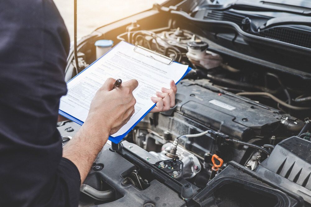 A Man is Writing on a Clipboard While Looking Under the Hood of a Car — JJE Automotive In Yarrawonga, NT