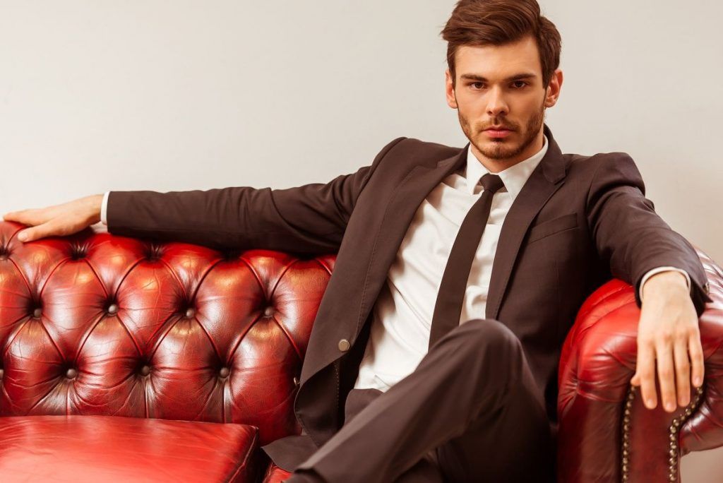 A man in a suit and tie is sitting on a red leather couch.