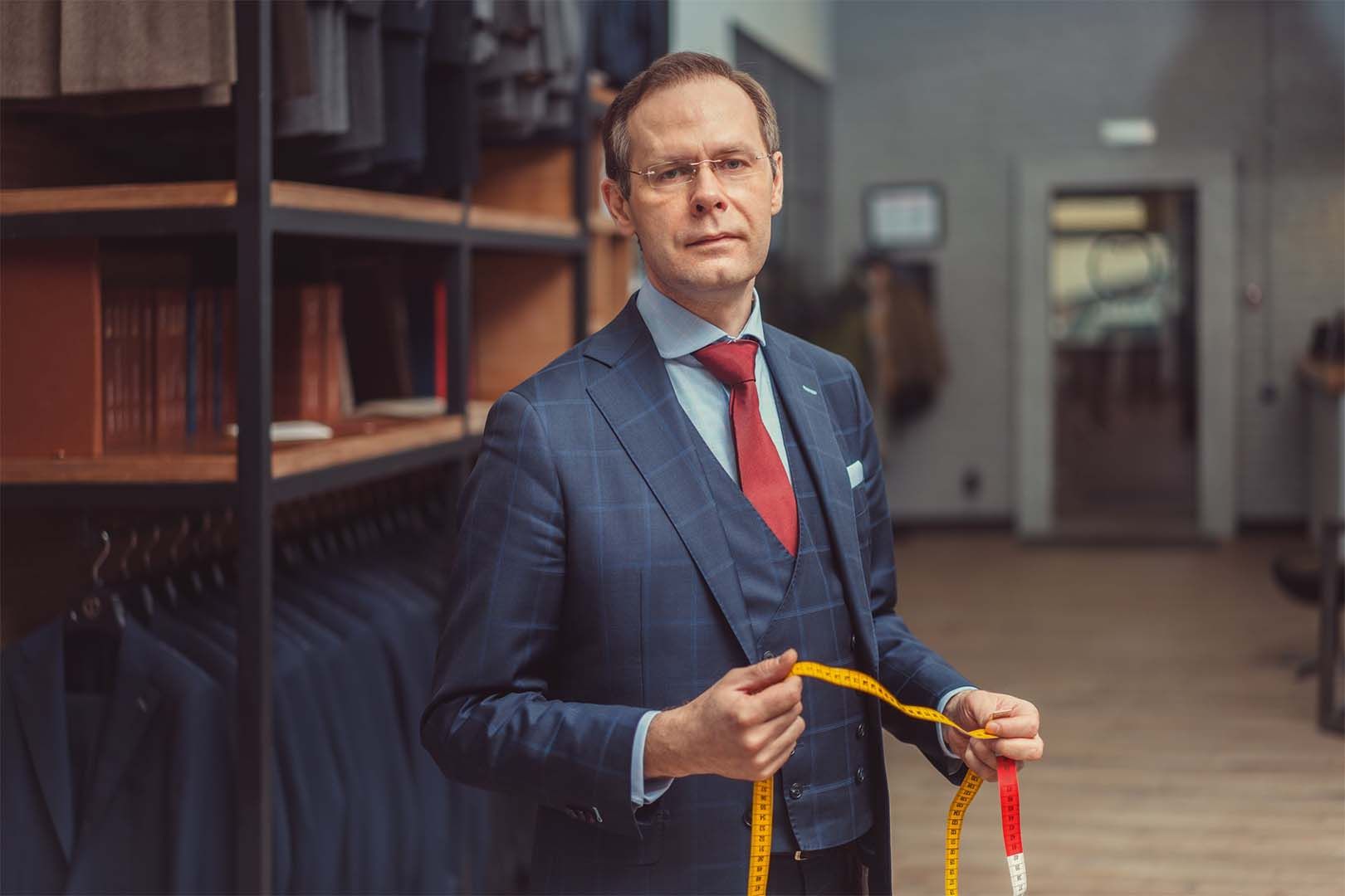 A man in a suit and tie is measuring himself with a tape measure.