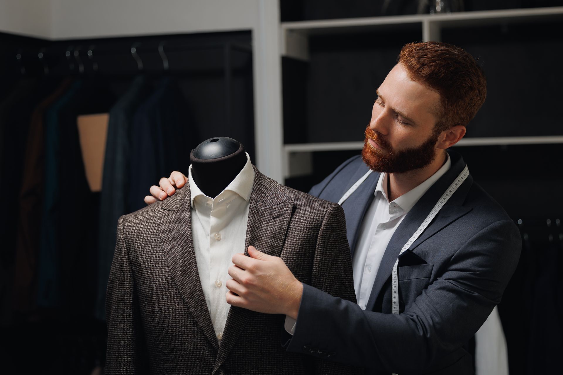 A man in a suit is measuring a jacket on a mannequin.