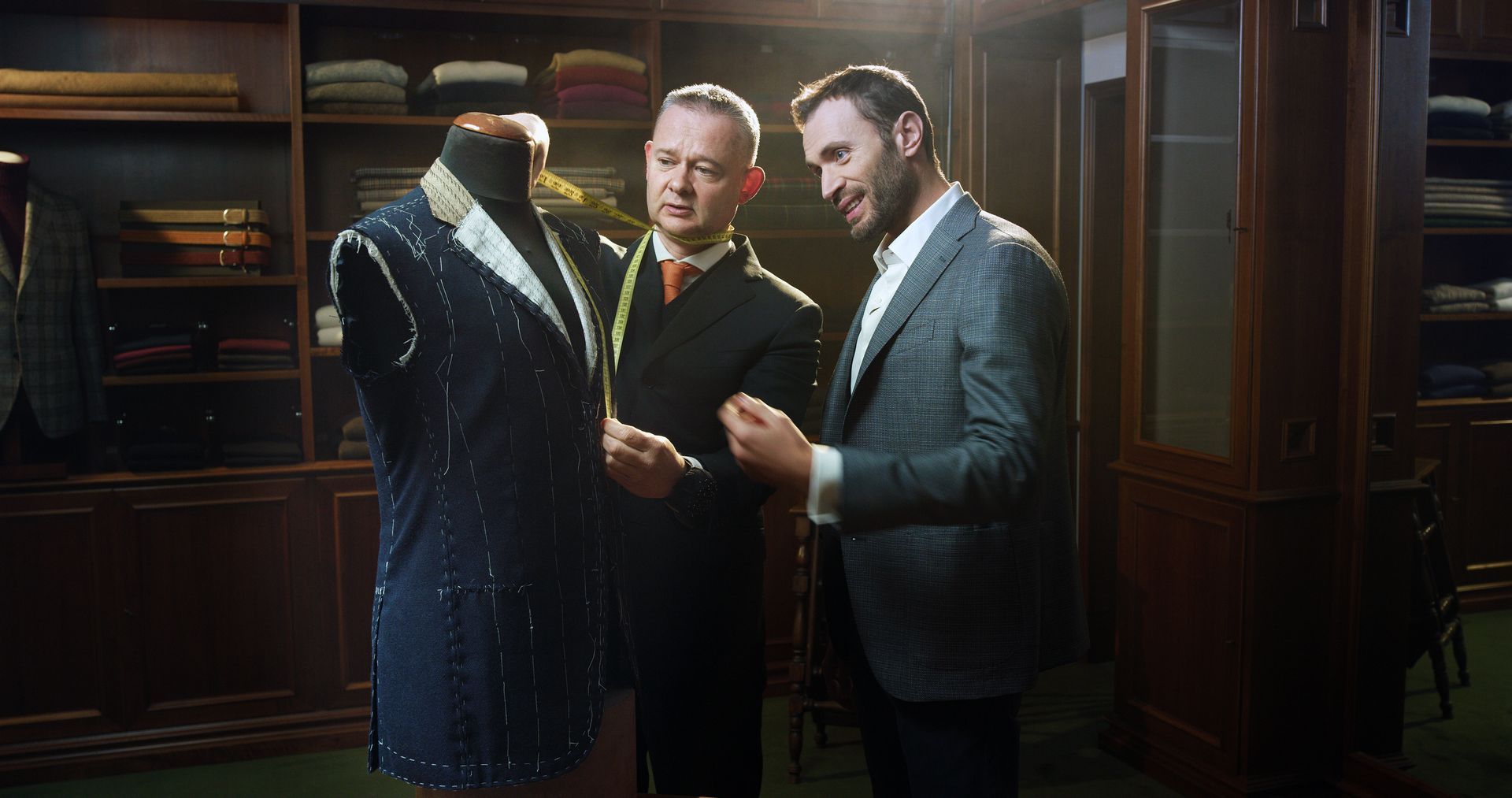 Two men are measuring a suit on a mannequin in a tailor shop.