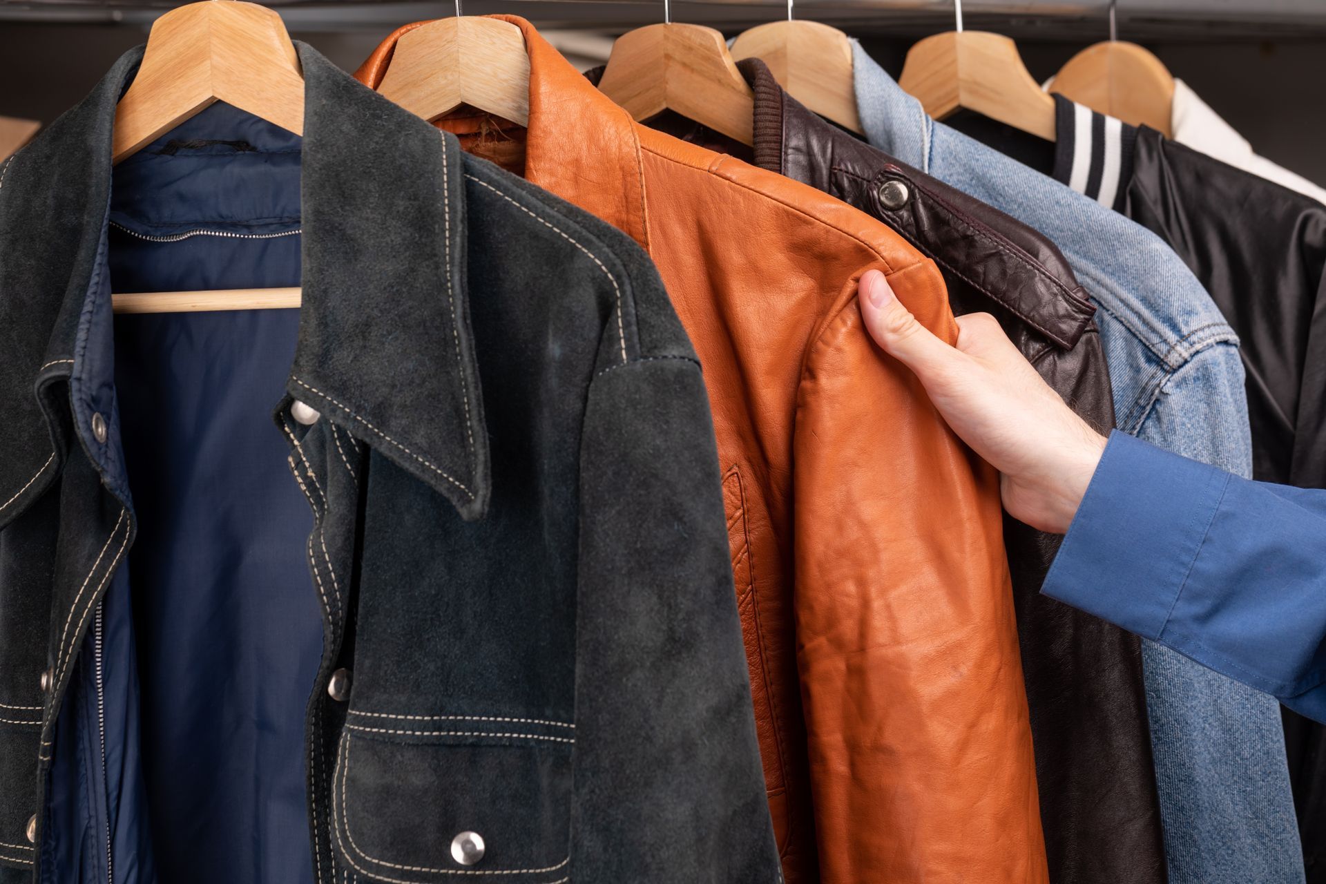 A person is reaching for a leather jacket in a closet
