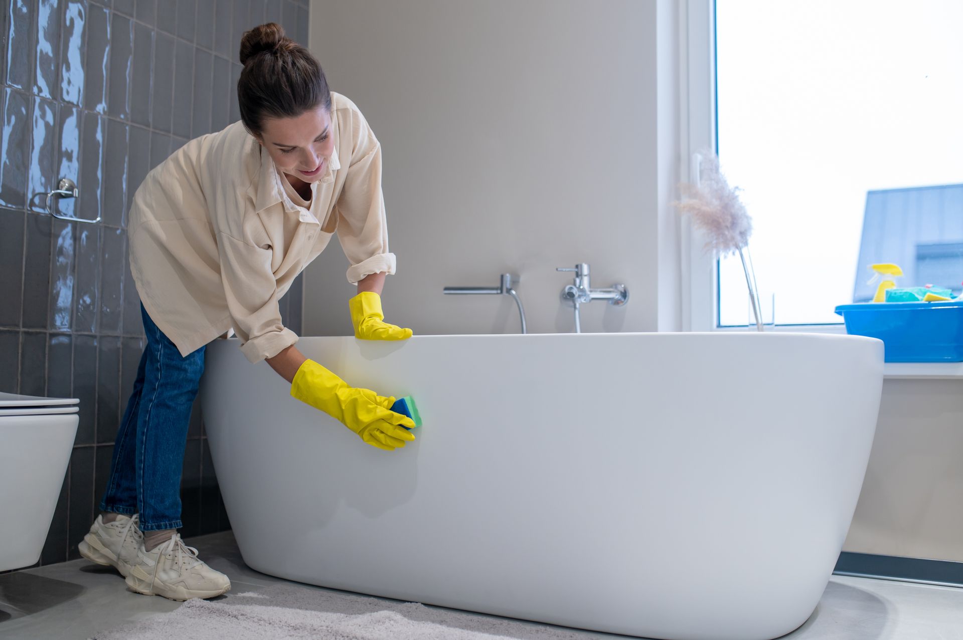 Une femme portant des gants jaunes nettoie une baignoire dans une salle de bain.