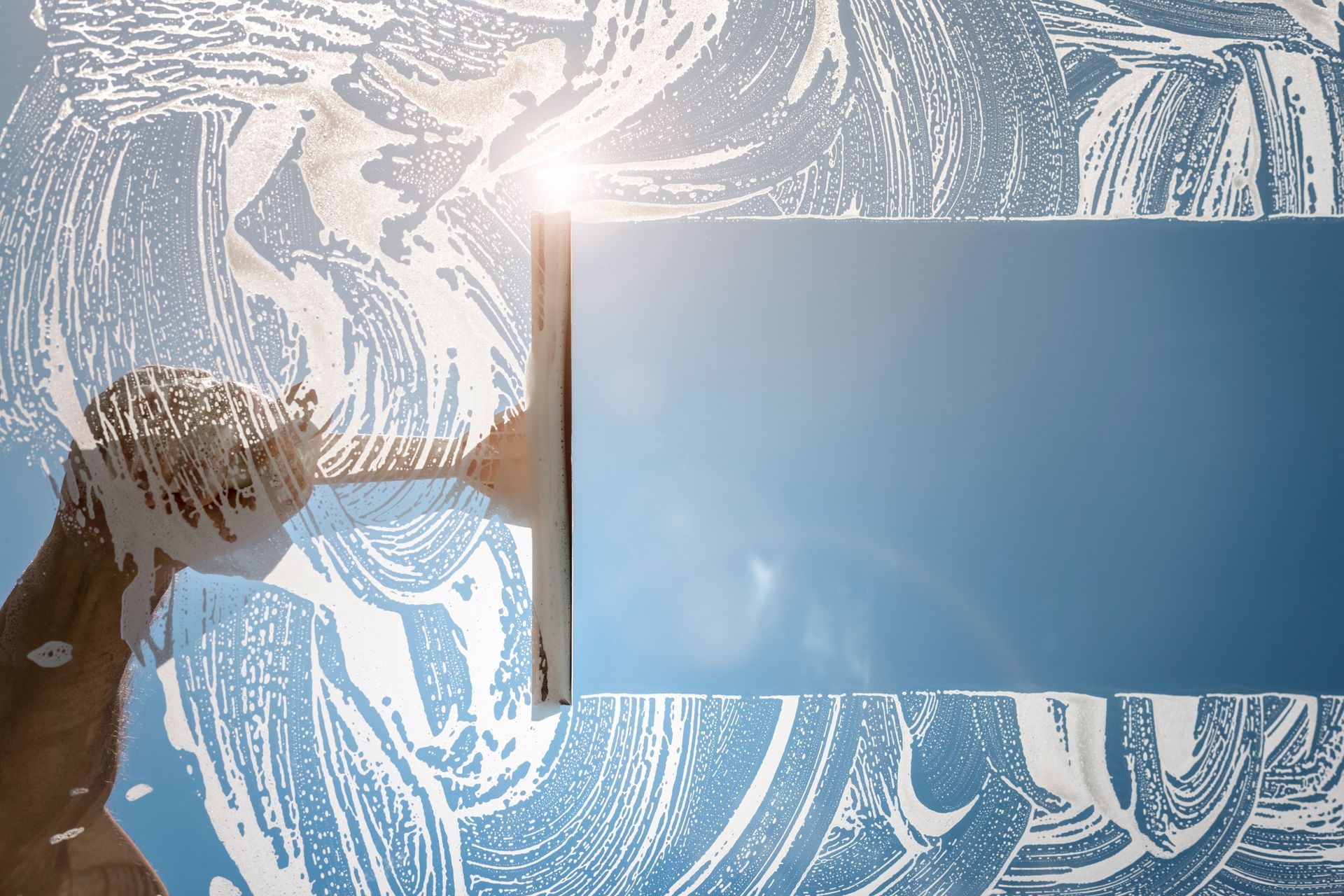 Personne lavant une fenêtre avec de la mousse, reflet du ciel lumineux, soleil.