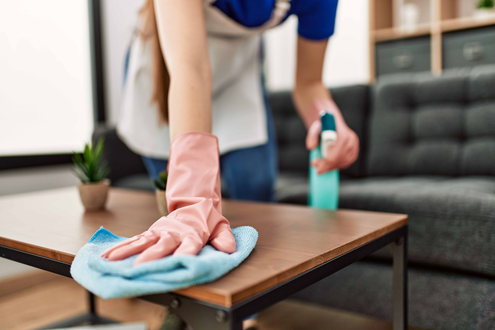 Une personne portant des gants bleus nettoie un comptoir de cuisine avec un vaporisateur.