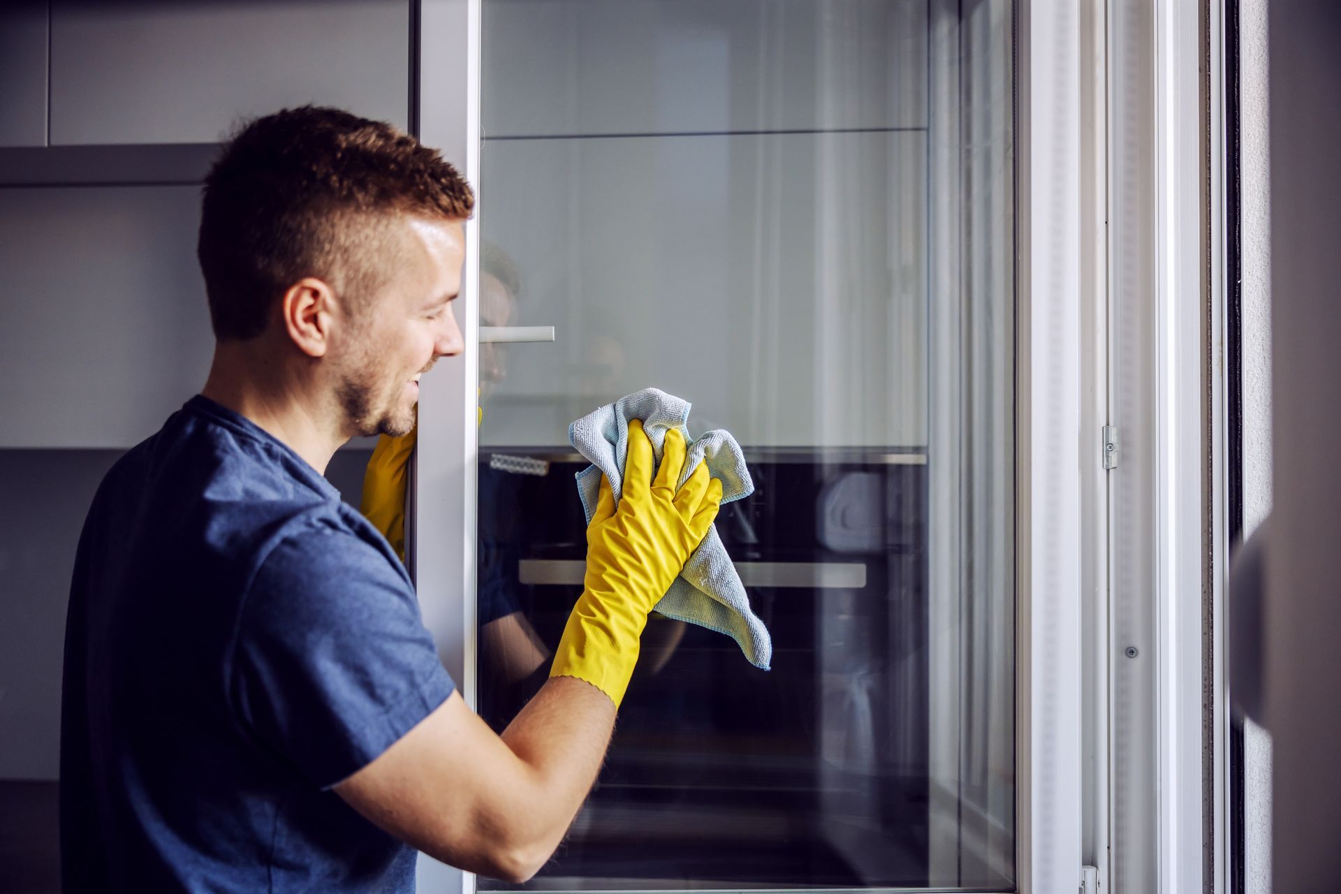 Un homme portant des gants jaunes nettoie la porte vitrée d'un four avec un chiffon.