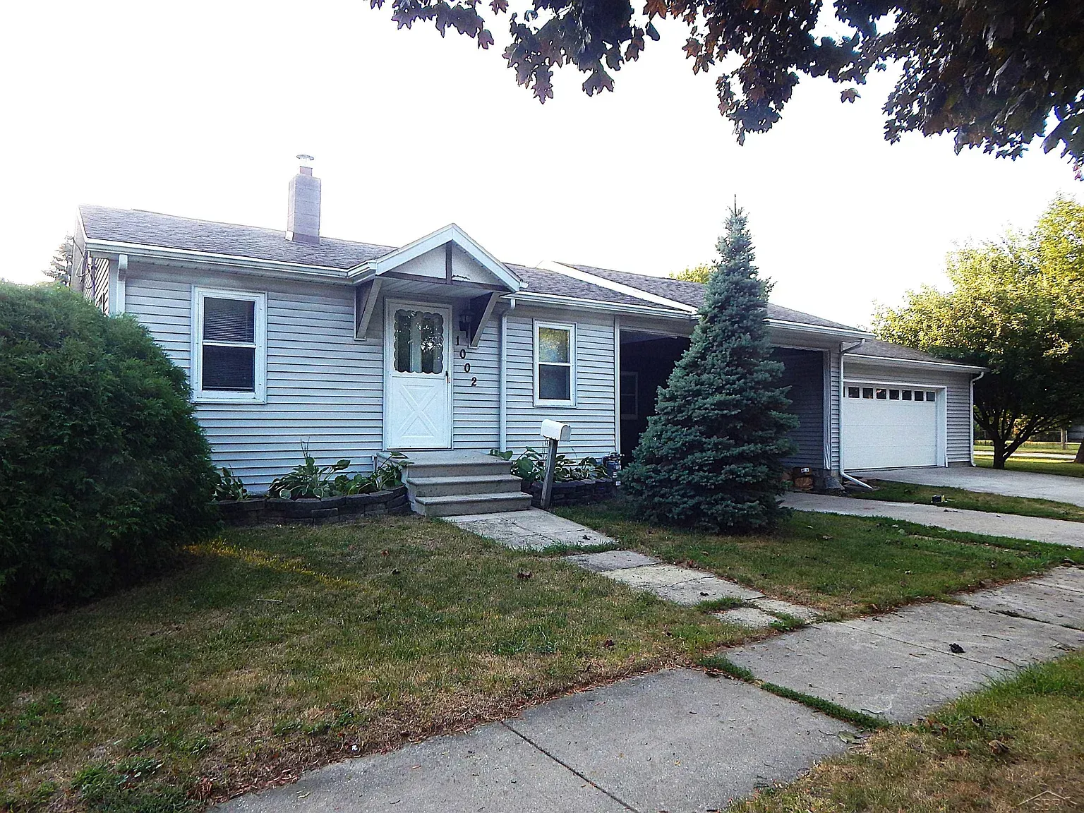 Single-story gray house with front porch, driveway, and lawn in a suburban neighborhood