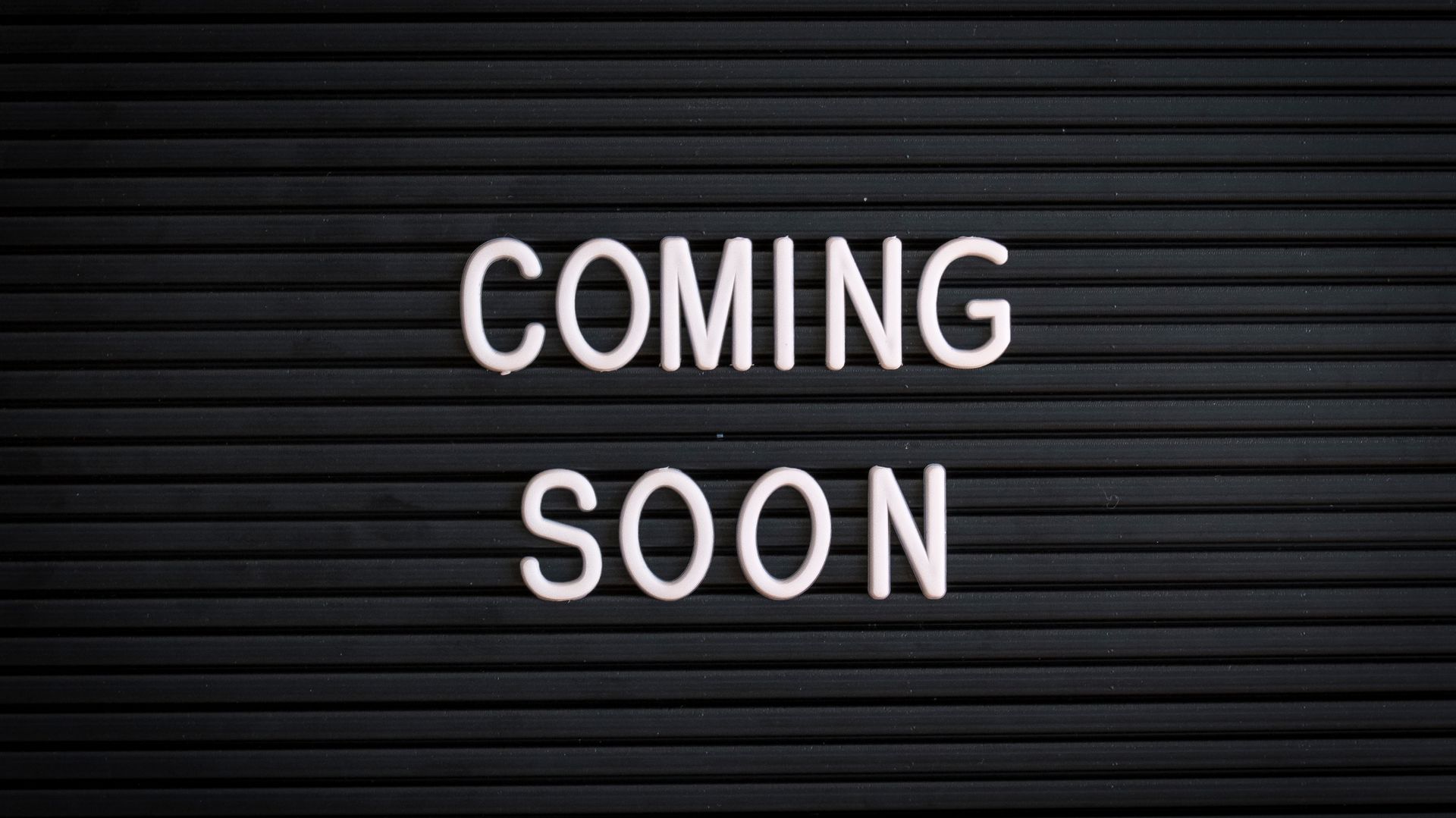 White “COMING SOON” text on a dark striped background.