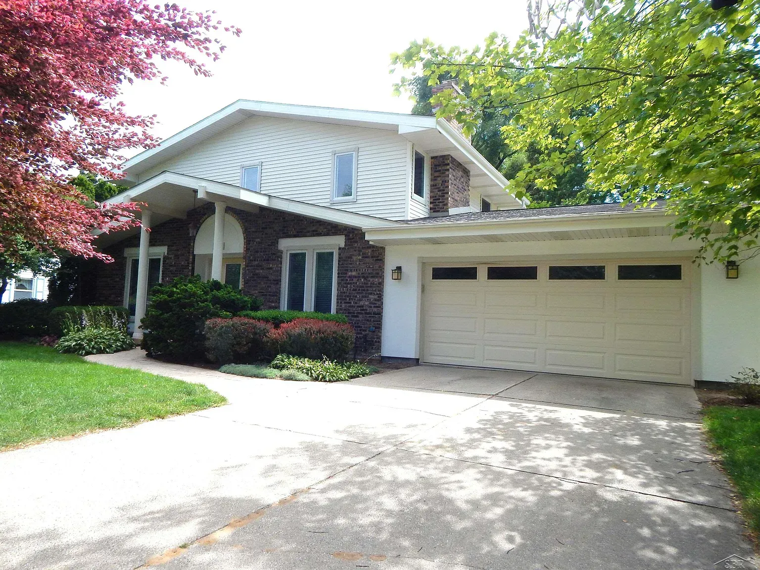 Suburban house with a double garage, front porch, and driveway shaded by trees.