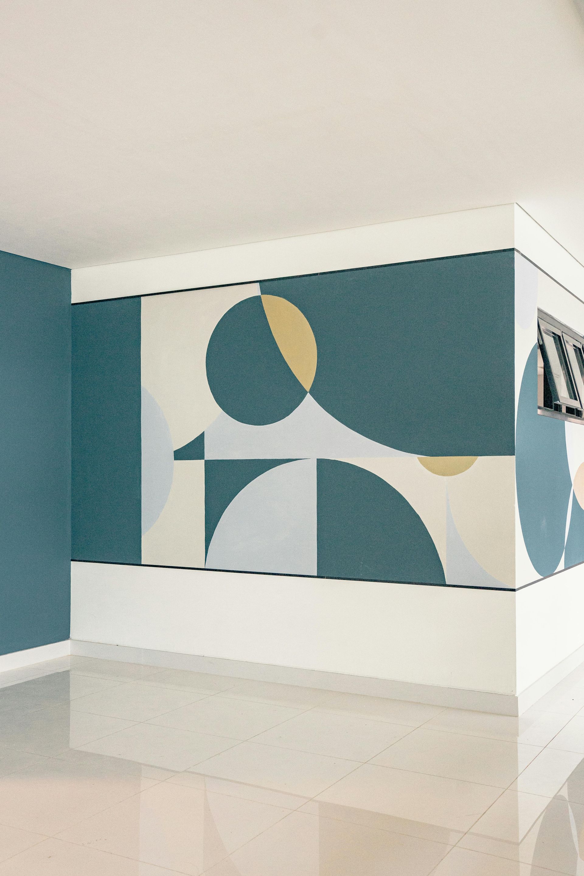 A wall mural featuring overlapping circles and geometric shapes in shades of teal, pale blue, cream, and mustard yellow.